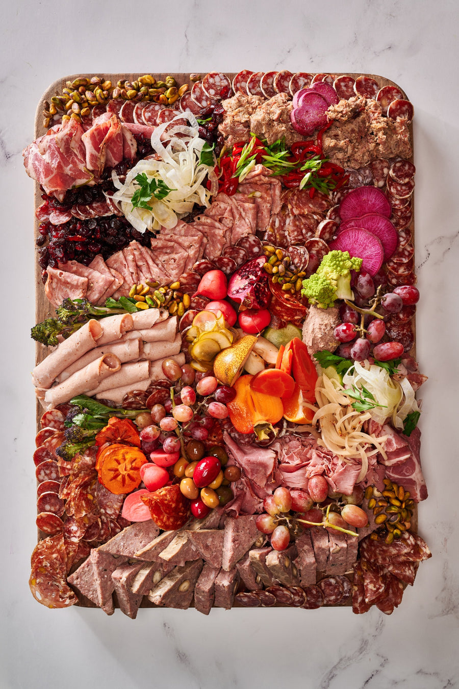 an olympia provions chefs choice board including but not limited to, ham, grapes, assortmens of salami, raisins, pistachios, potatos, carrots, olives, and pomegranates