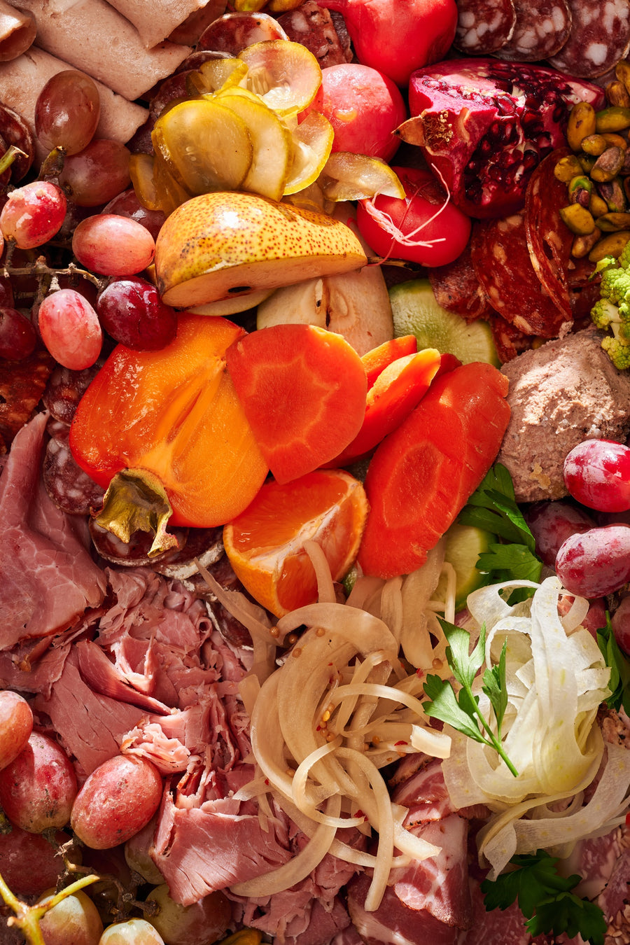 an olympia provions chefs choice board including but not limited to, ham, grapes, assortmens of salami, raisins, pistachios, potatos, carrots, olives, and pomegranates