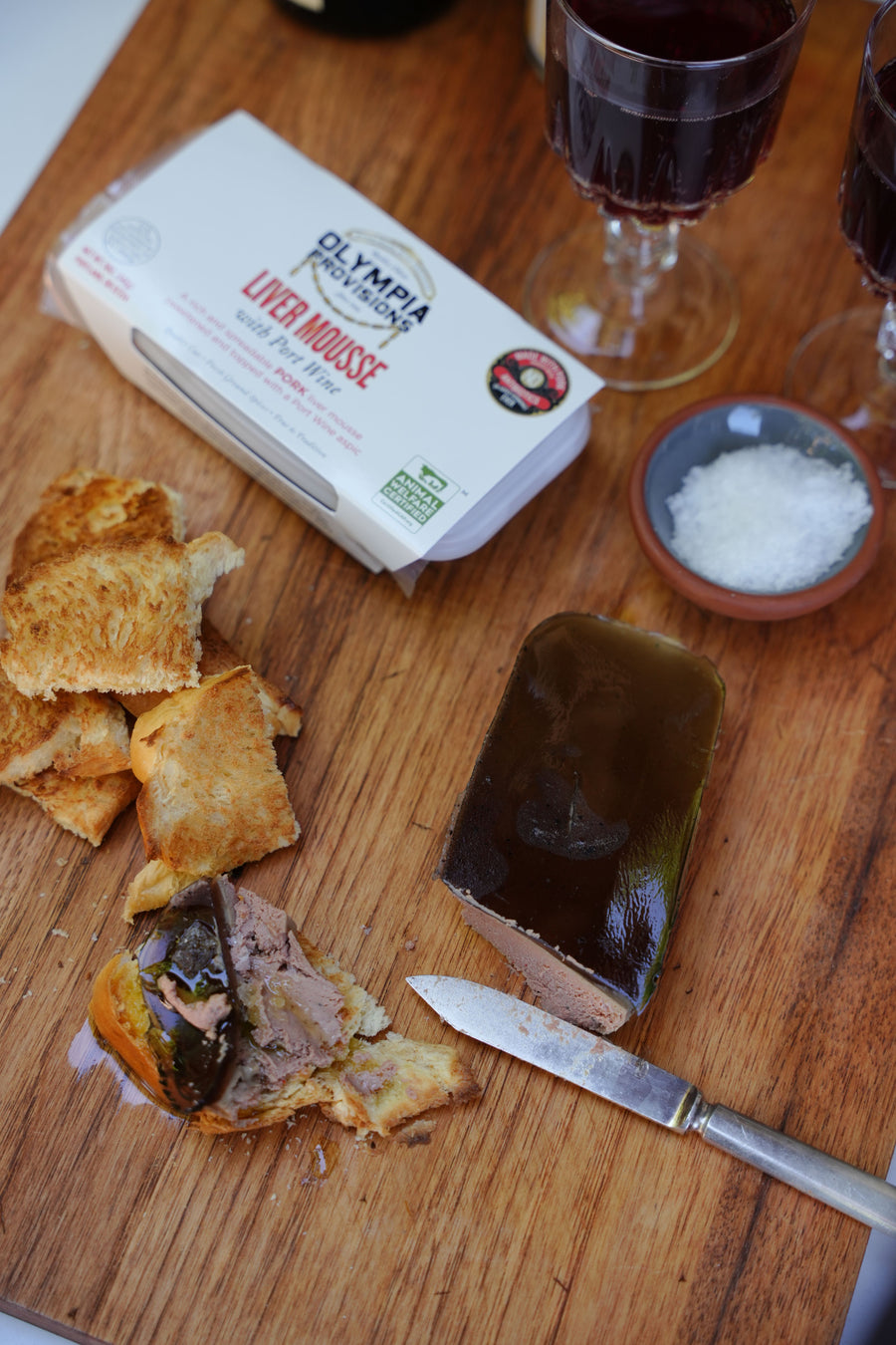 Olympia Liver Mousse on a wooden board with toasted bread and red wine.