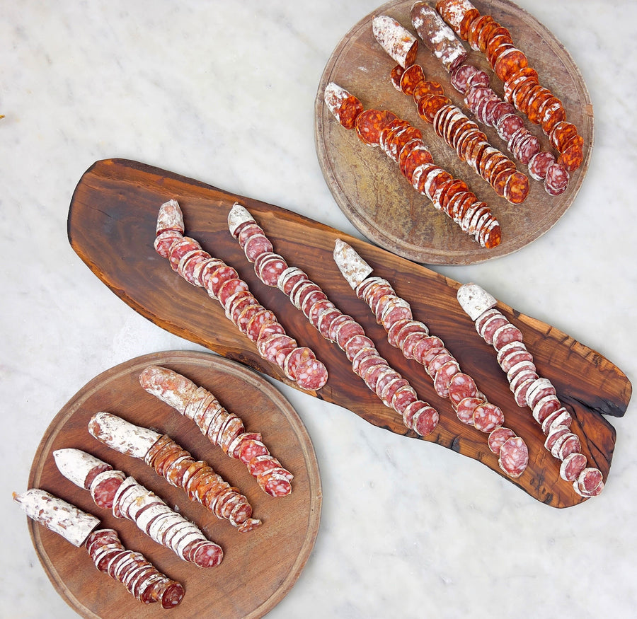 A variety of sliced salamis arranged on wooden boards, showcasing different colors and seasoning.