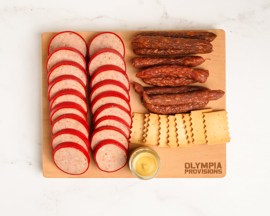 Wooden cutting board with peperettes, saumer sausage, and crackers on a white background.
