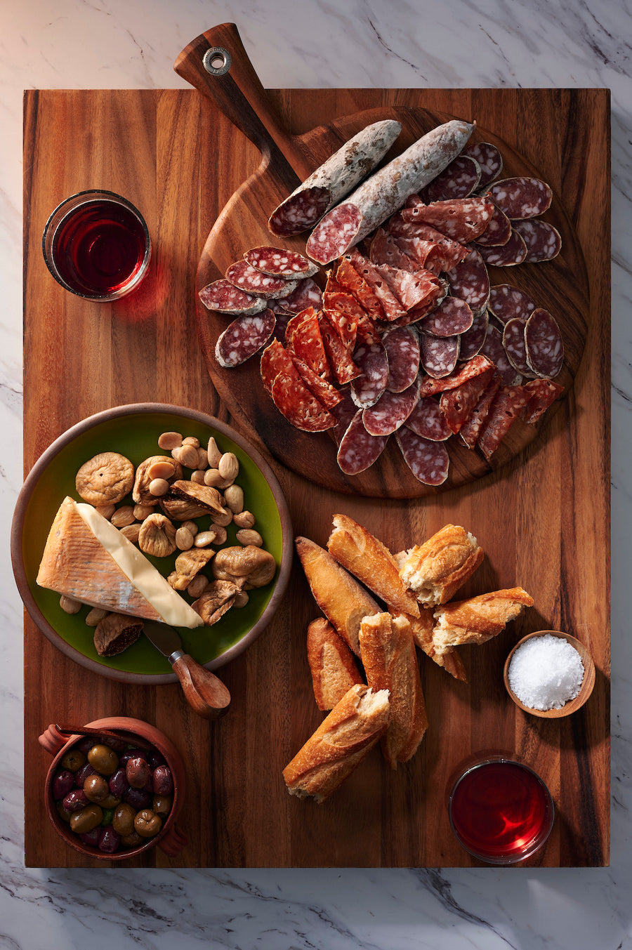 rustic charcuterie board set on a wooden surface. The board features a variety of sliced cured meats, including olympia provisions cacciatore salami and chorizo