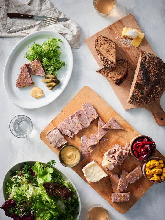 Wooden cutting board with sliced pate, bread, and pickles.